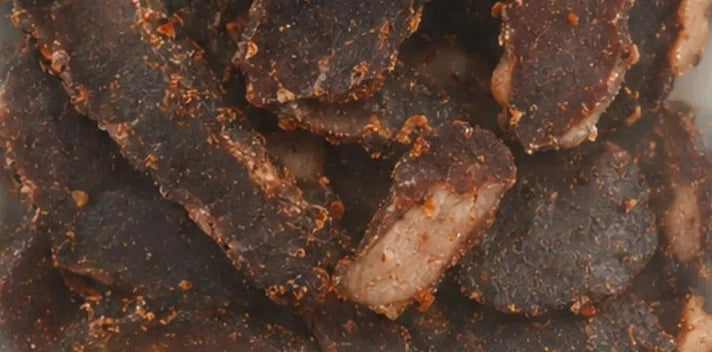 African Heat biltong seen through the pack window: dark air-dried beef with visible seasoning